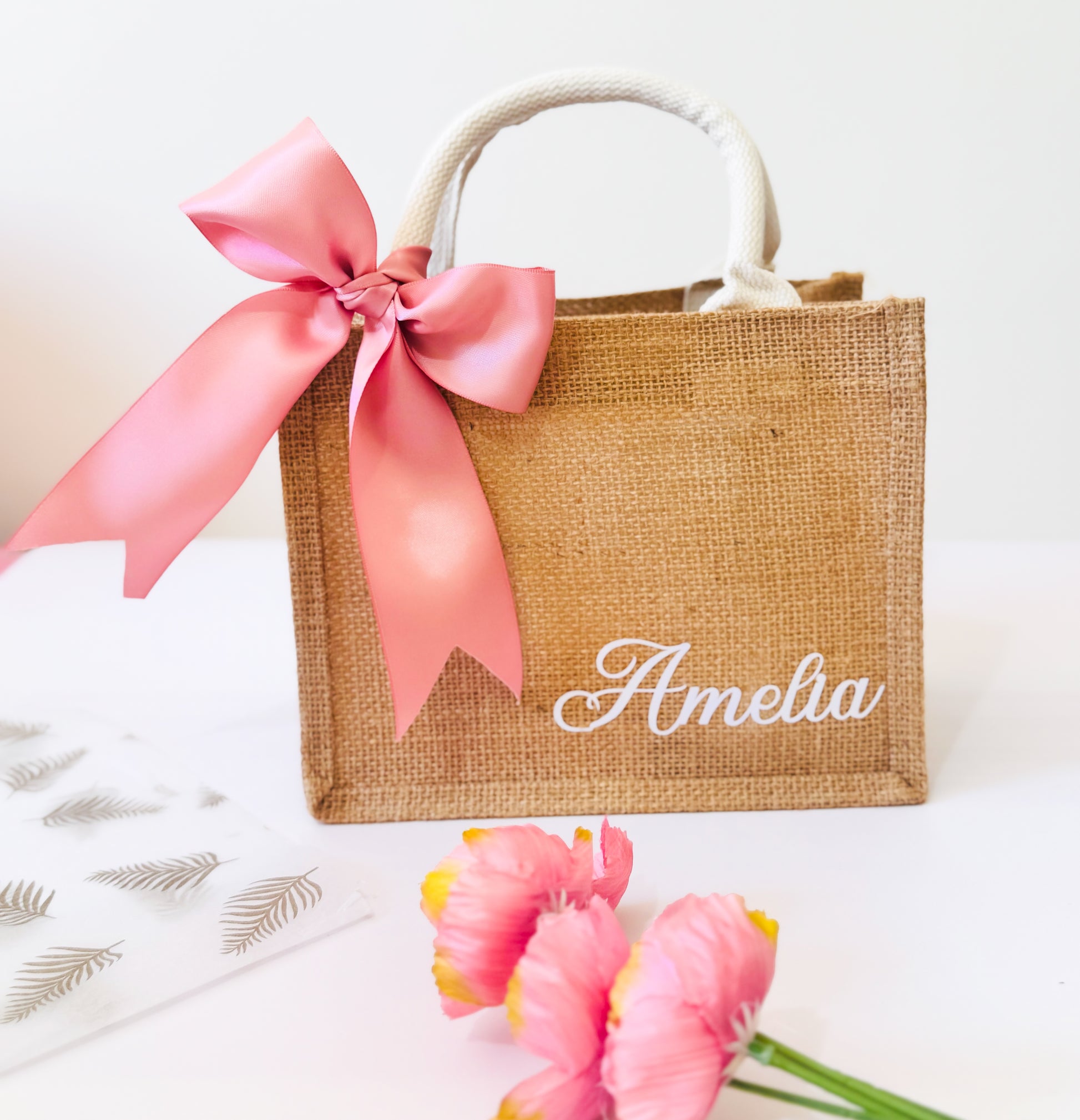 Jute bag with pink ribbon and 'Amelia' branding on a white background