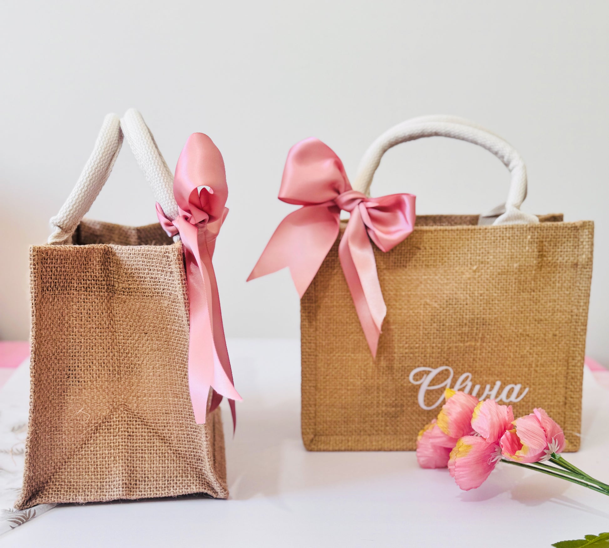 Two jute bags with pink ribbons and a name on a light background