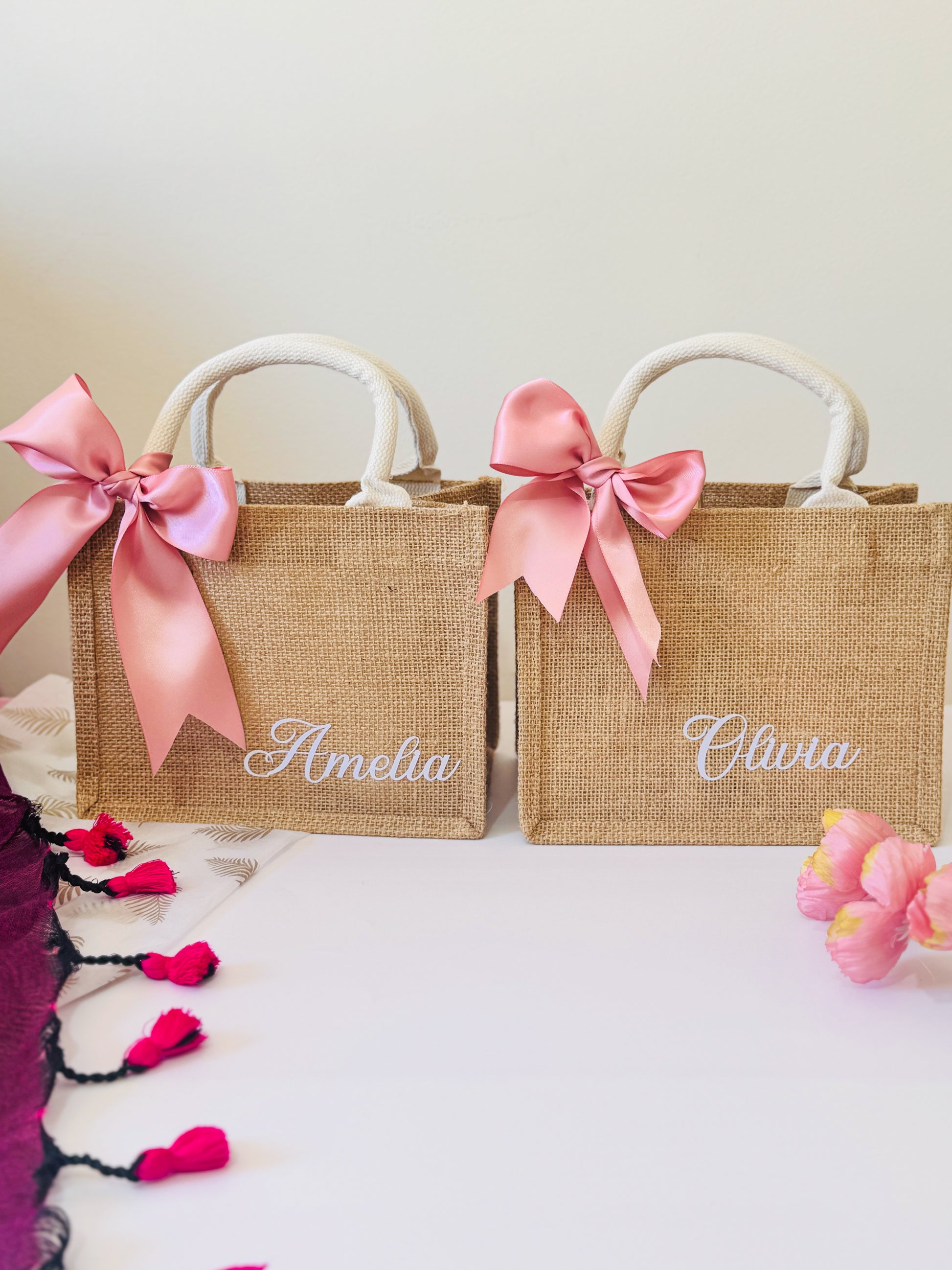 Two jute bags with pink ribbons and personalized names on a light background